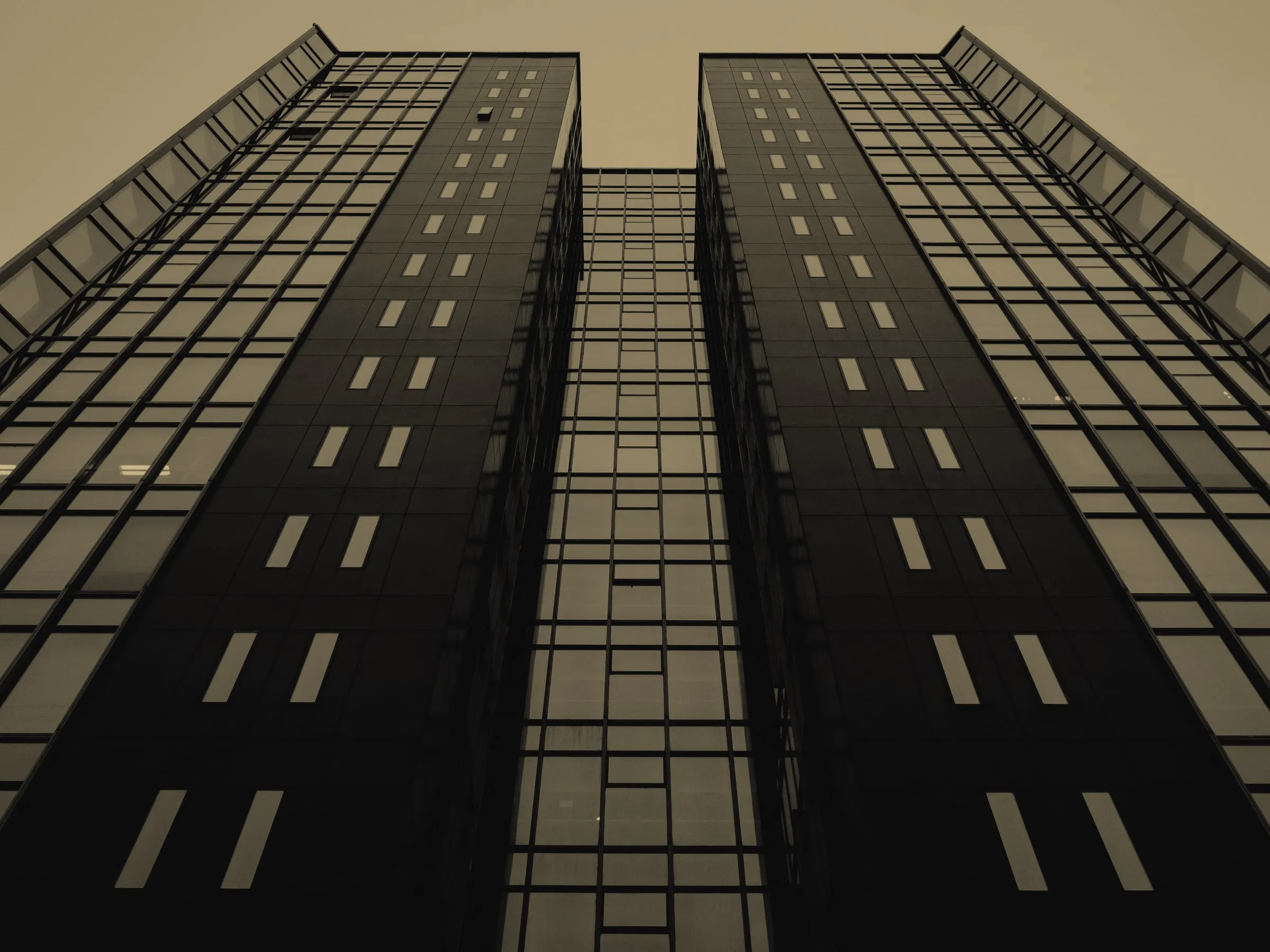 Two dark glass towers rising into a pale sky, seen from street level.