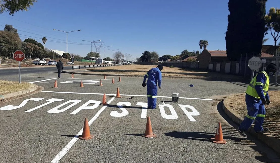 Workers paint large white STOP legends at a road intersection.